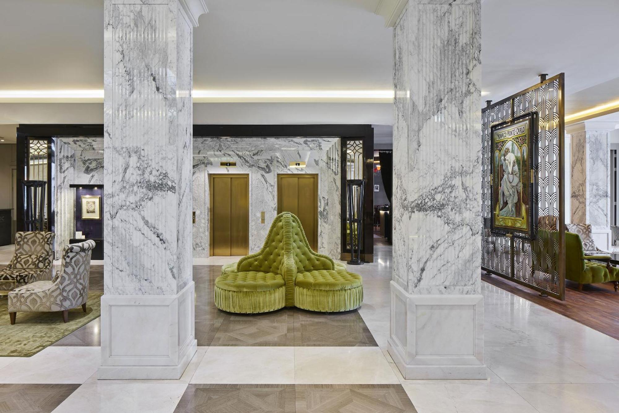 Titanic Gendarmenmarkt Berlin Extérieur photo The photo depicts a luxurious hotel lobby featuring elegant marble columns and flooring. To the center, there is a unique, plush green seating arrangement shaped like a stylized, abstract form. In the background, gold elevator doors are visible, comp