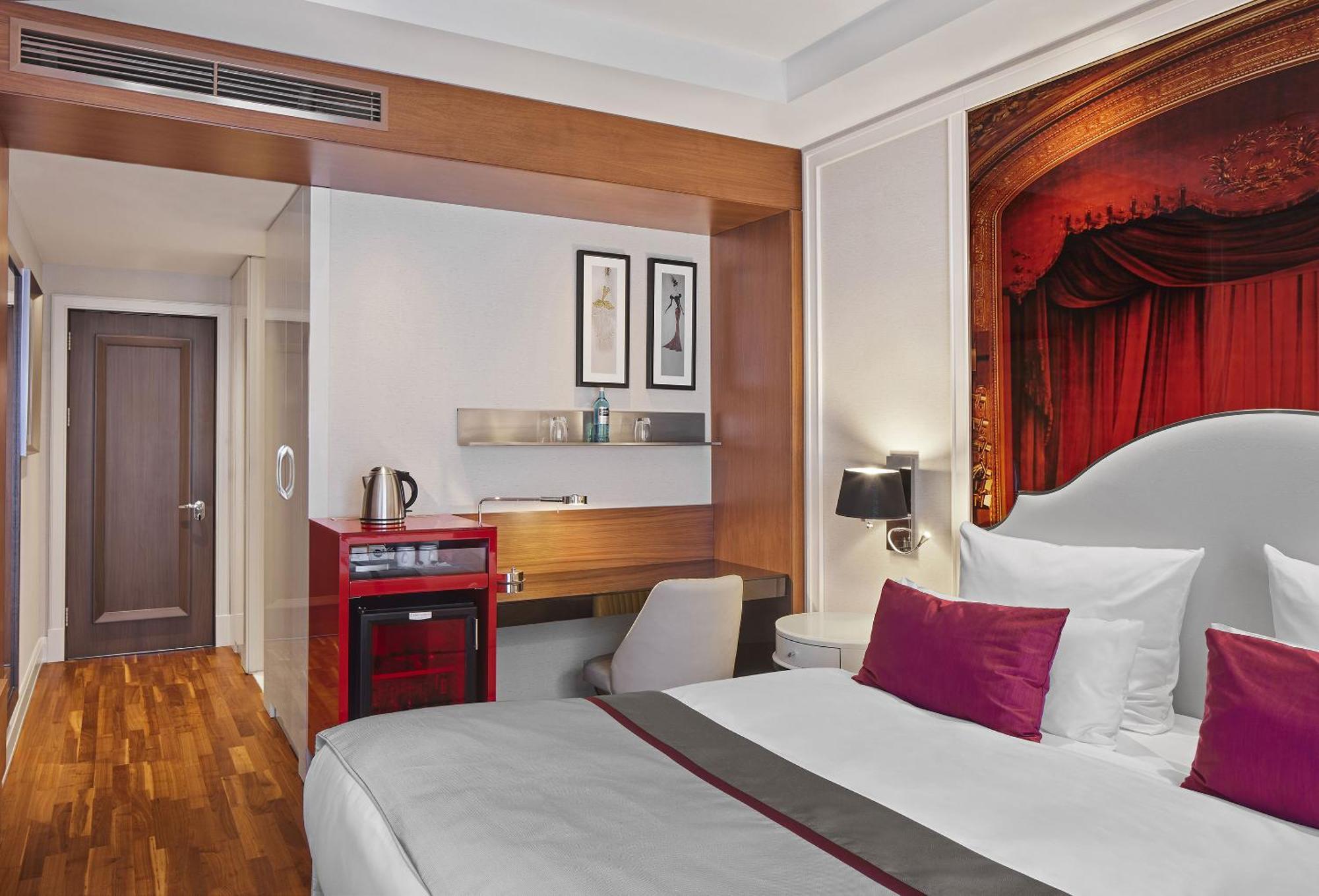 Titanic Gendarmenmarkt Berlin Extérieur photo The photo depicts a modern hotel room featuring a queen-sized bed with white linens and decorative pillows in shades of purple. The room has wooden flooring and a stylish design, with a combination of light and warm colors. 

To one side, there is a 